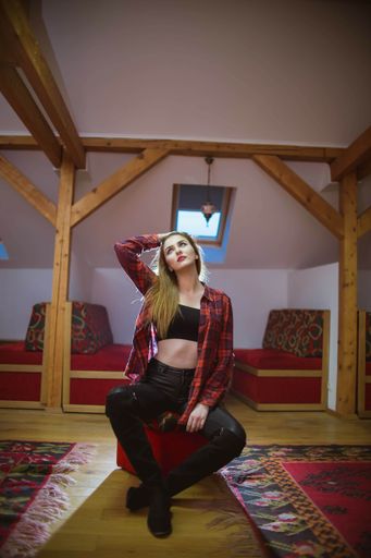 A vertical shot of a sexy caucasian female in a flannel shirt sitting on an ottoman indoors