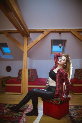 A young lady with blonde hair wearing a red shirt and posing on the chair