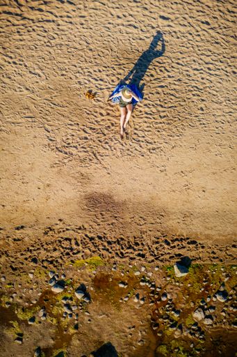 An aerial shot of a female sitting on her jacket on the Baltic seashore with green sea algae on stones