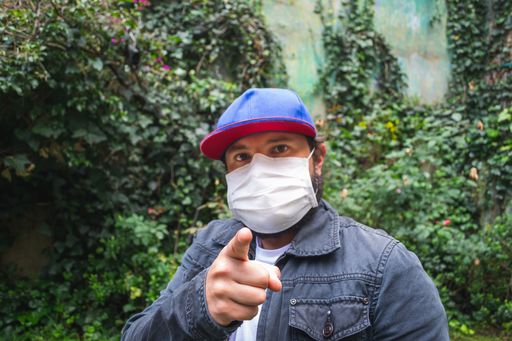 A man in a blue cap pointing at you wearing a white face mask to protect from dust and coronavirus