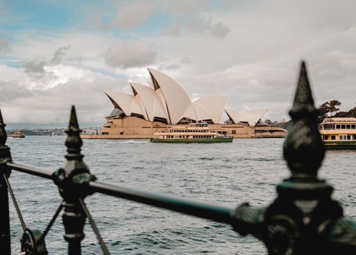 A vibrant view of the iconic opera house across a tranquil body of water, with a black metal fence in the foreground