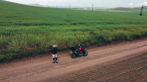 A man on motorcycle riding on a dirt road in a rural setting