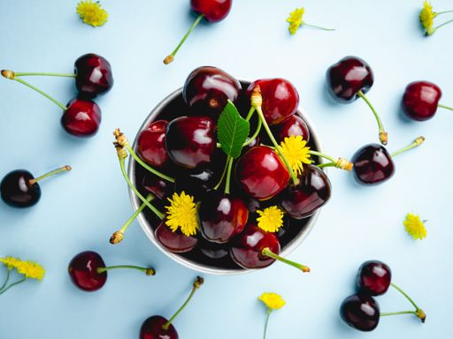 A top view of fresh juicy cherries with flowers in a bowl isolated on a blue background