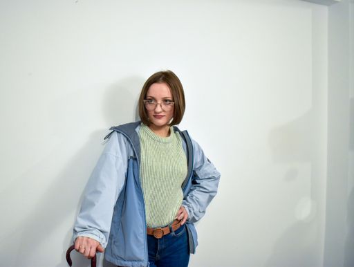 A young Caucasian woman in a green sweater and blue jacket holding a red umbrella.