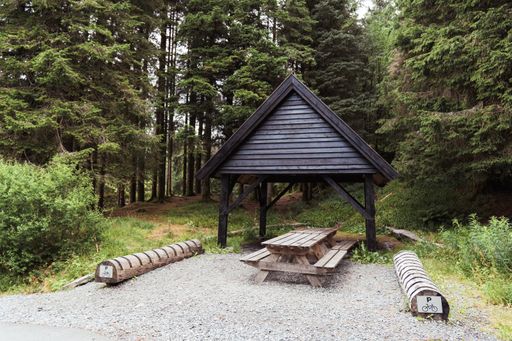 A traditional wooden picnic table, complete with benches in the shade of a rustic wooden shelter.