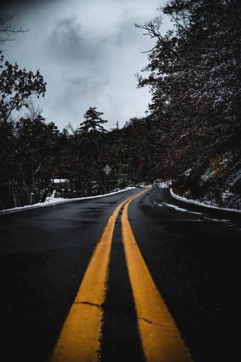 A dark road illuminated by a street light with two yellow lines.