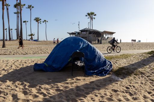 A tent with a tarp over it sits on the beach near the Venice Beach boardwalk. Homeless people have tents set up all along the boardwalk