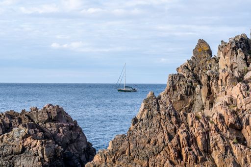 A boat is sailing in a tranquil ocean, passing by an impressive rocky cliff in Varberg, Sweden