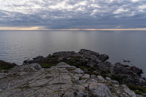 A scenic seascape featuring a rocky shoreline, with wispy clouds gathering in the sky above in Varberg, Sweden