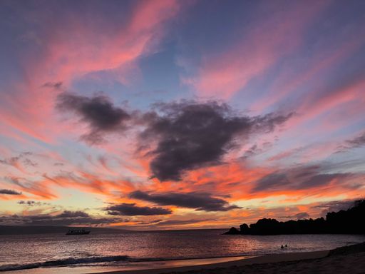 A breathtaking view of the sun setting over the beach with a picturesque sky filled with fluffy, white clouds