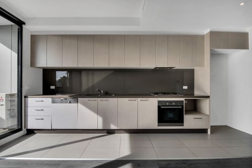 A kitchen with beige wooden furniture and gray laminate flooring