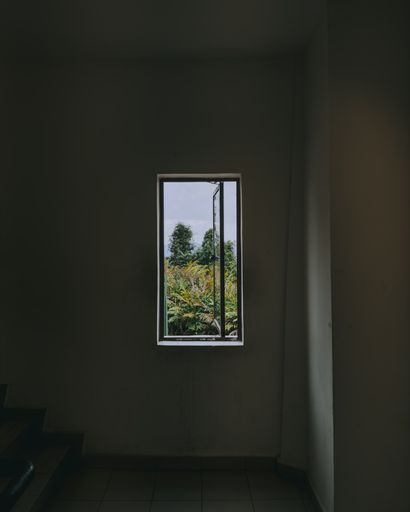An empty room interior with white tiled flooring and a small window at the back, illuminated by natural light