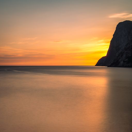 A picturesque view of a vibrant sunset over the sea with a large rocky formation in Lofoten, Norway