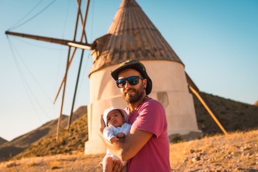 A young father with his newborn son enjoying a vacation in San Jose, Spain with mills in background