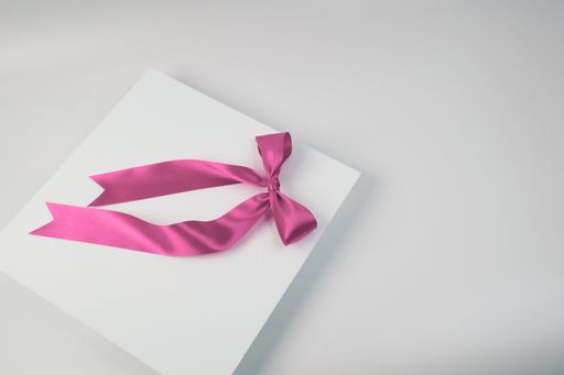 A white gift box, tied with a pink ribbon, sits against a white background