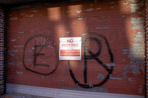 A vivid red and black sign on a brick wall with graffiti nearby