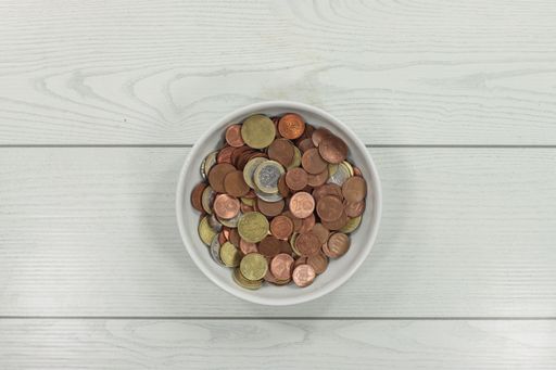 An overhead shot of euro coins in a white bowl on a white wooden surface