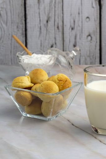A vertical closeup shot of a bowl of biscuits next to a glass of milk on a white wooden table