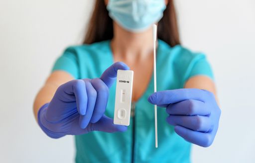 Selective focus image of medical worker wearing blue scrubs holding rapid sars-cov-2 covid antigen test and swab.