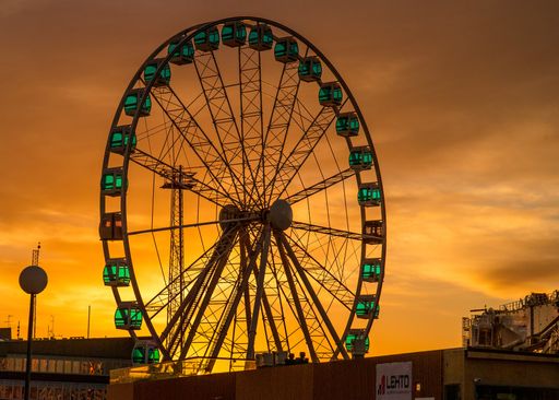 A closeup shot of a Ferris wheel with a beautiful skyline at sunset in the background
