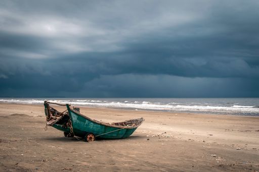 An old wooden fishing boat on a beach against a backdrop of tumultuous grey clouds