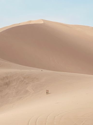 A person climbing a dune in a vast desert