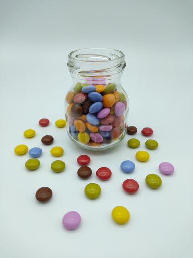 A vertical shot of small colorful candies and a glass jar on an isolated background