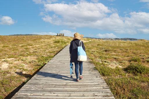 A girl with a straw hat, clothes, and a bag walking along a wooden path