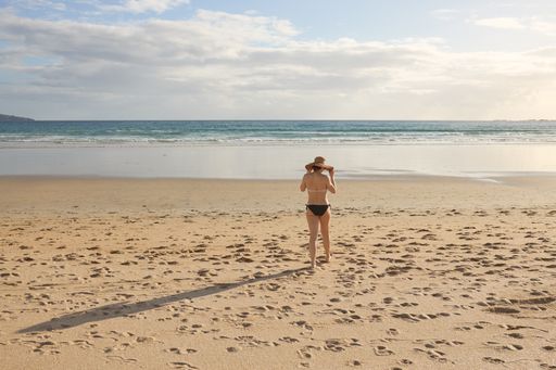 A girl in a bikini and a straw hat walking on the shore of a beach
