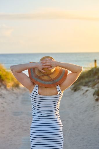 A closeup shot of a girl with a straw hat on a path to the beach
