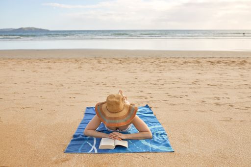 A girl lying on a towel and reading a book on the beach