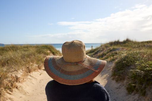 A girl with a straw hat and a black coat on a path to the beach