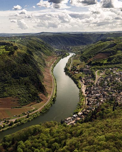An aerial shot of a wide river surrounded by tree-covered hills and a small village