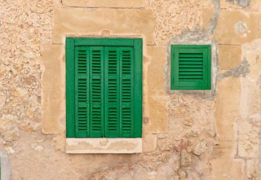A closeup shot of green windows on an exterior wall of an old building