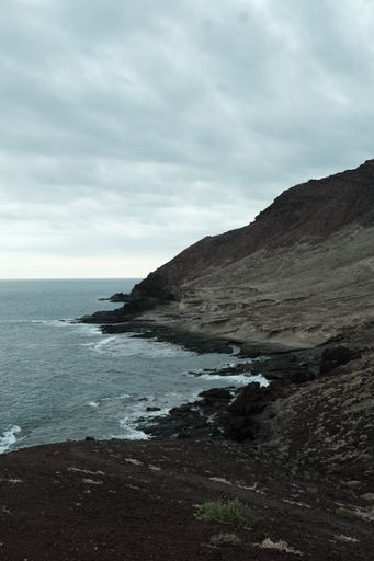 A tranquil seascape featuring a beach with rocky formations and lush green grass, stretching from the edge of the ocean to the sandy shore