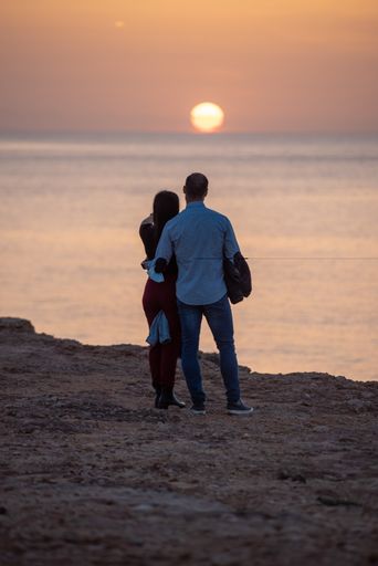 A back view of a young couple enjoying a sunset in Cala Saona beach, Formentera, Spain