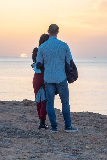 A back view of a young couple enjoying a sunset in Cala Saona beach, Formentera, Spain