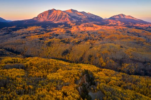 An aerial landscape view of two distant mountain ranges with a foreground of lush green trees