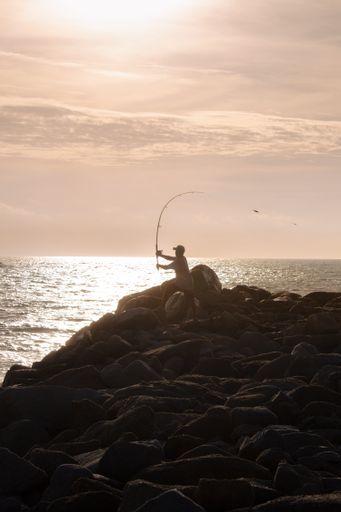A vertical shot of a fisherman casting a rod near a picturesque body of water at sunset
