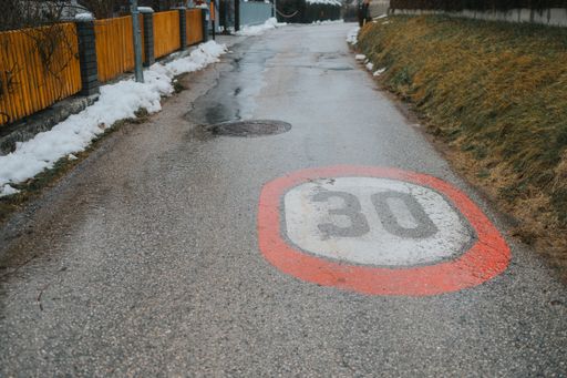 A red and white street sign painted on an asphalt pavement in a suburban area