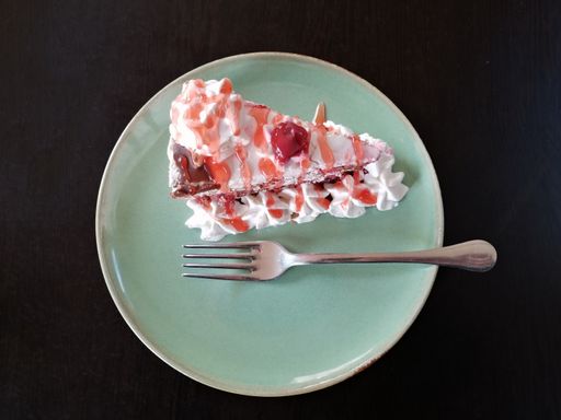 A top view of a piece of cake with cream and cherry with fork on green plate