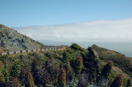 A landscape of hills covered in greenery and a road surrounded by the sea under the sunlight