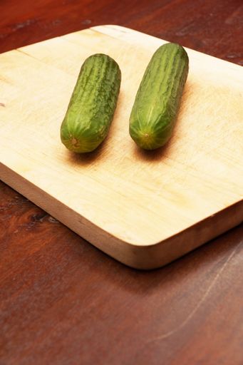 A vertical shot of two cucumbers on a wooden cutting board