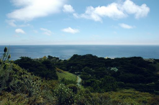 A landscape of hills covered in greenery and a road surrounded by the sea under the sunlight