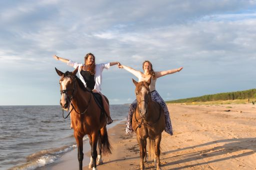 Two young female friends happily posing together on horses on a sandy beach