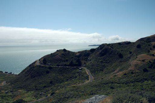 A landscape of hills covered in greenery and a road surrounded by the sea under the sunlight