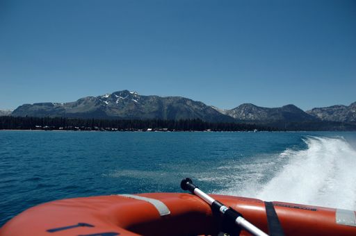 A red kayak riding through the sea surrounded by hills under the sunlight and a blue sky