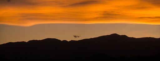 A panoramic silhouette of a mountain range under an orange cloudy sunset sky