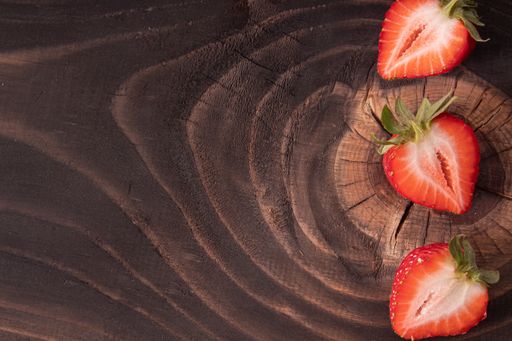 An overhead shot of strawberries cut in half on a dark wooden surface