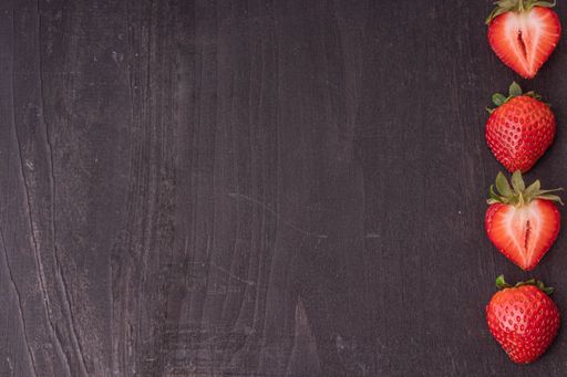 An overhead shot of strawberries cut in half on a dark wooden surface